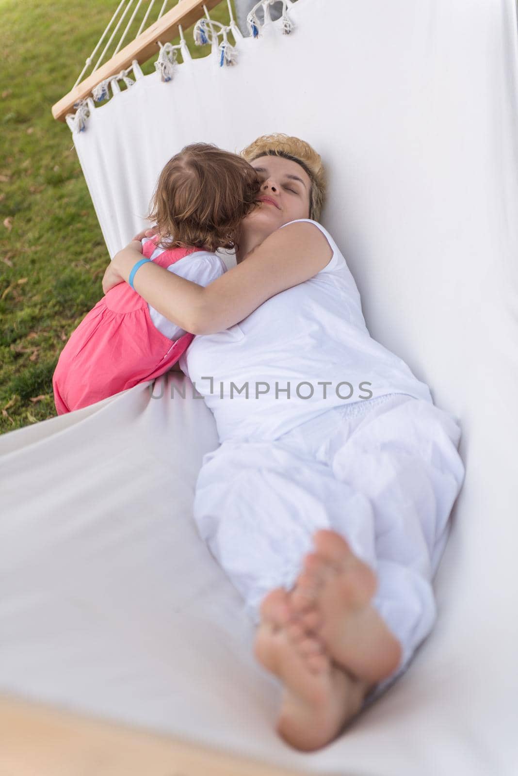 Happy mother and a little daughter enjoying free time hugging and relaxing in a hammock during a sunny day on holiday home garden