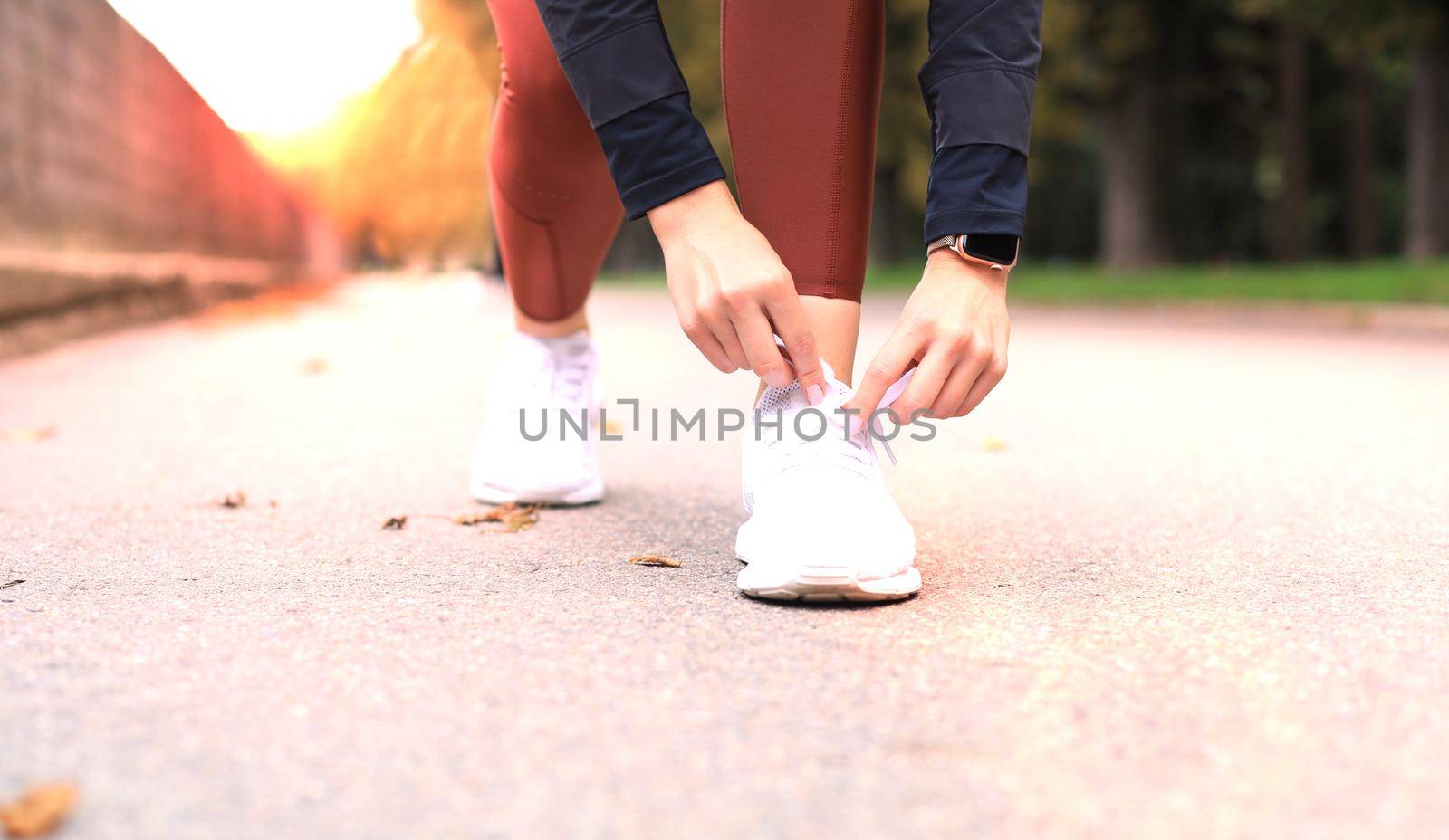 Closeup of unrecognizable sport woman tying sports shoes during evening run outdoors. by tsyhun