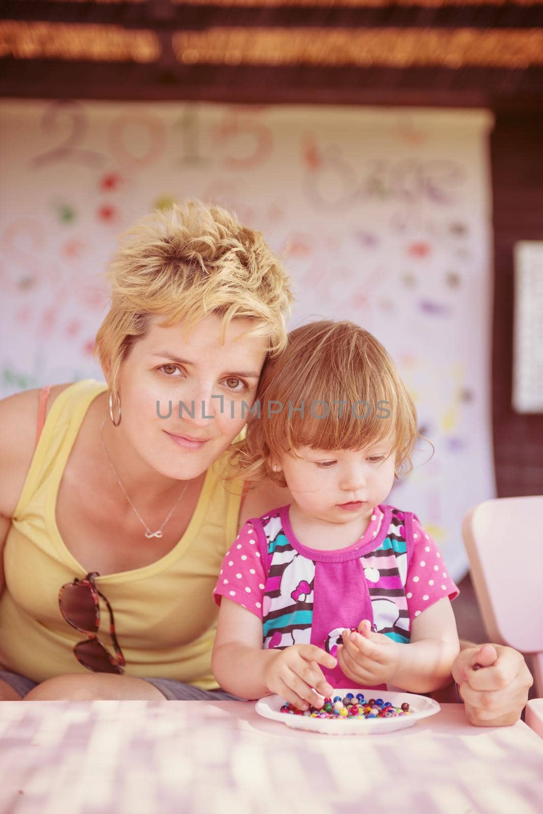 cute little girl making jewelry with  her mother in creative outdoor playground