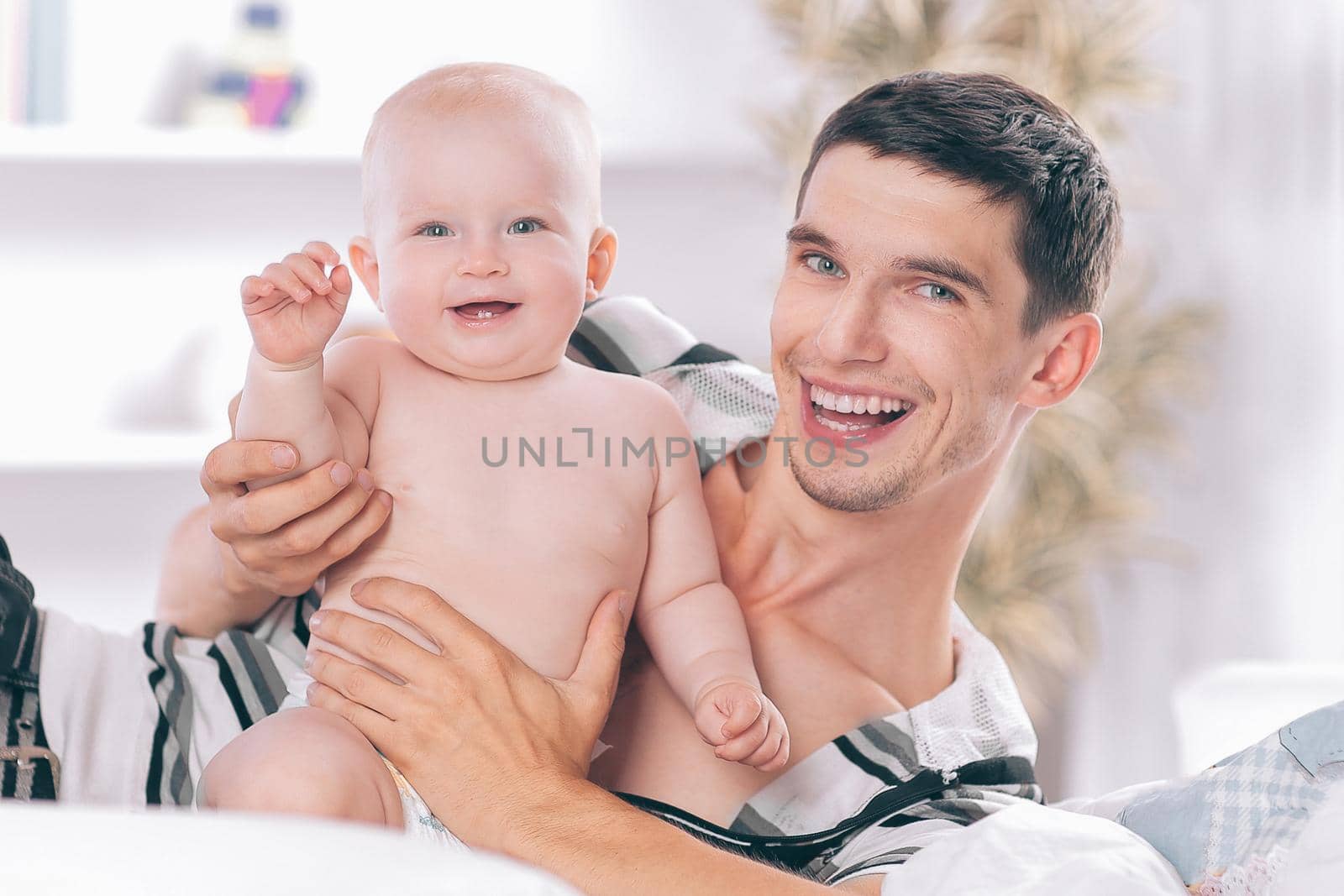 happy young father playing with baby on sofa at home