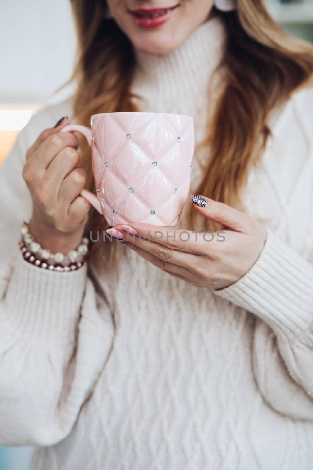 Close-up stock photo of a young fair-haired woman holding a cute coffee cup with golden design and text be mine . Morning coffee in a beautiful coffee cup.