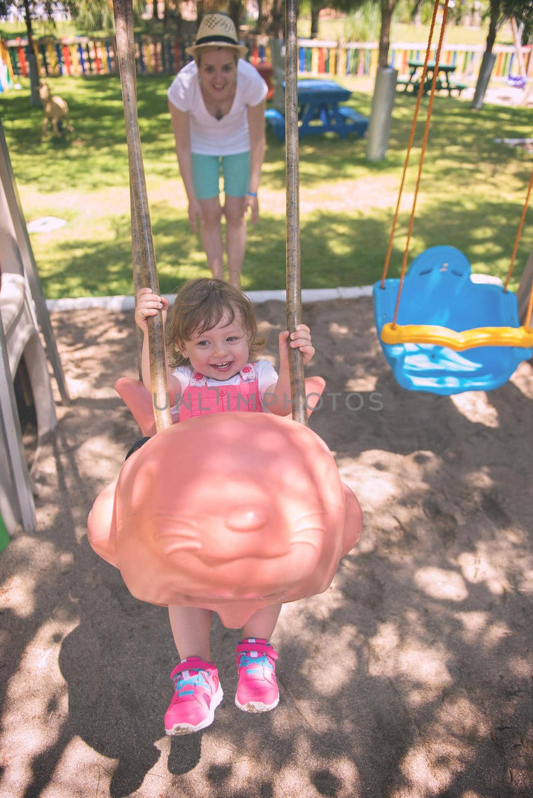 young mother and her little daughter smiling together while swinging at the playground in the park