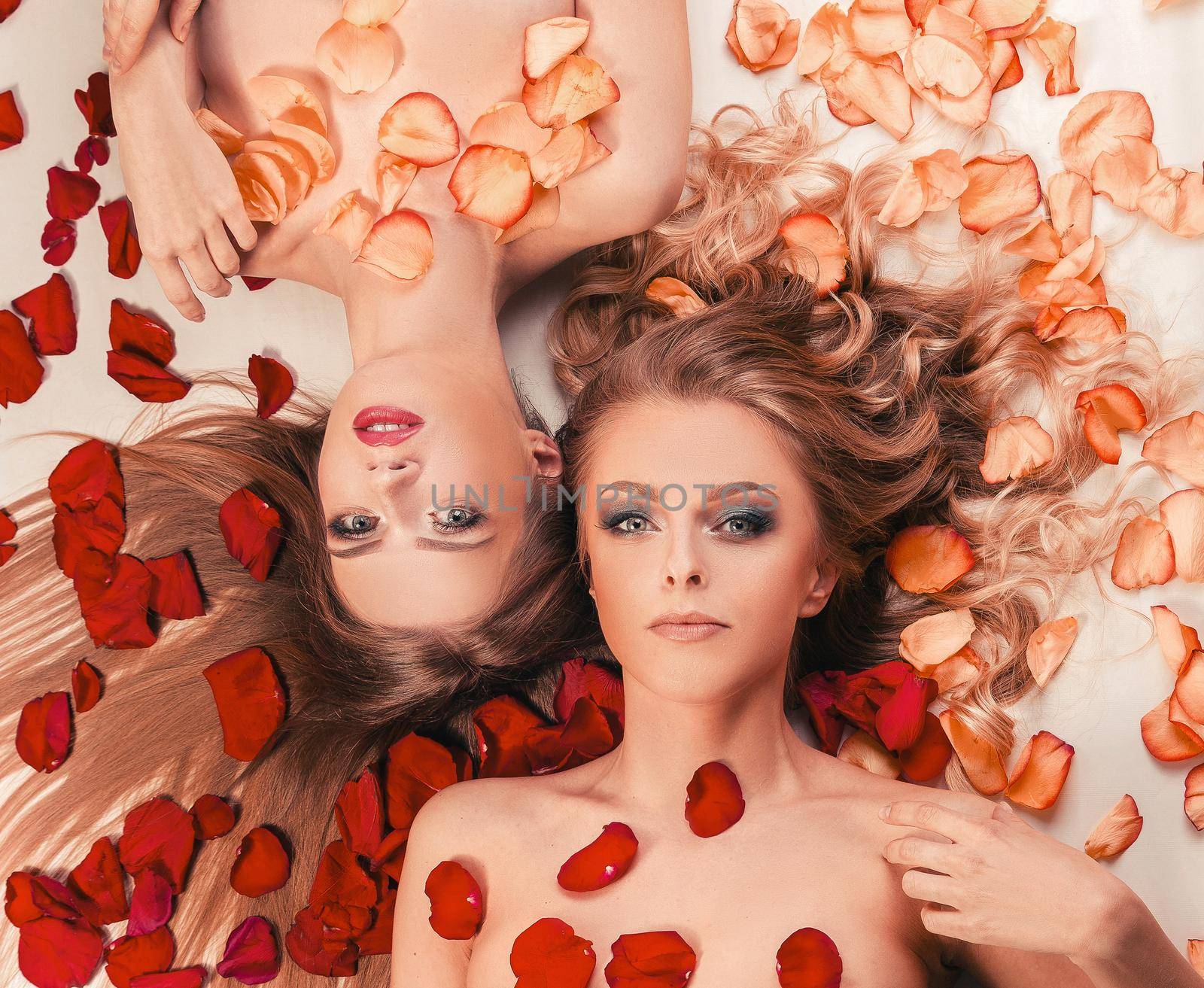 two beautiful young women relaxing lying among rose petals. the concept of a healthy lifestyle