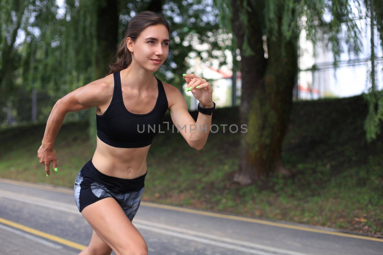 Young woman in sports clothing running while exercising outdoors. by tsyhun