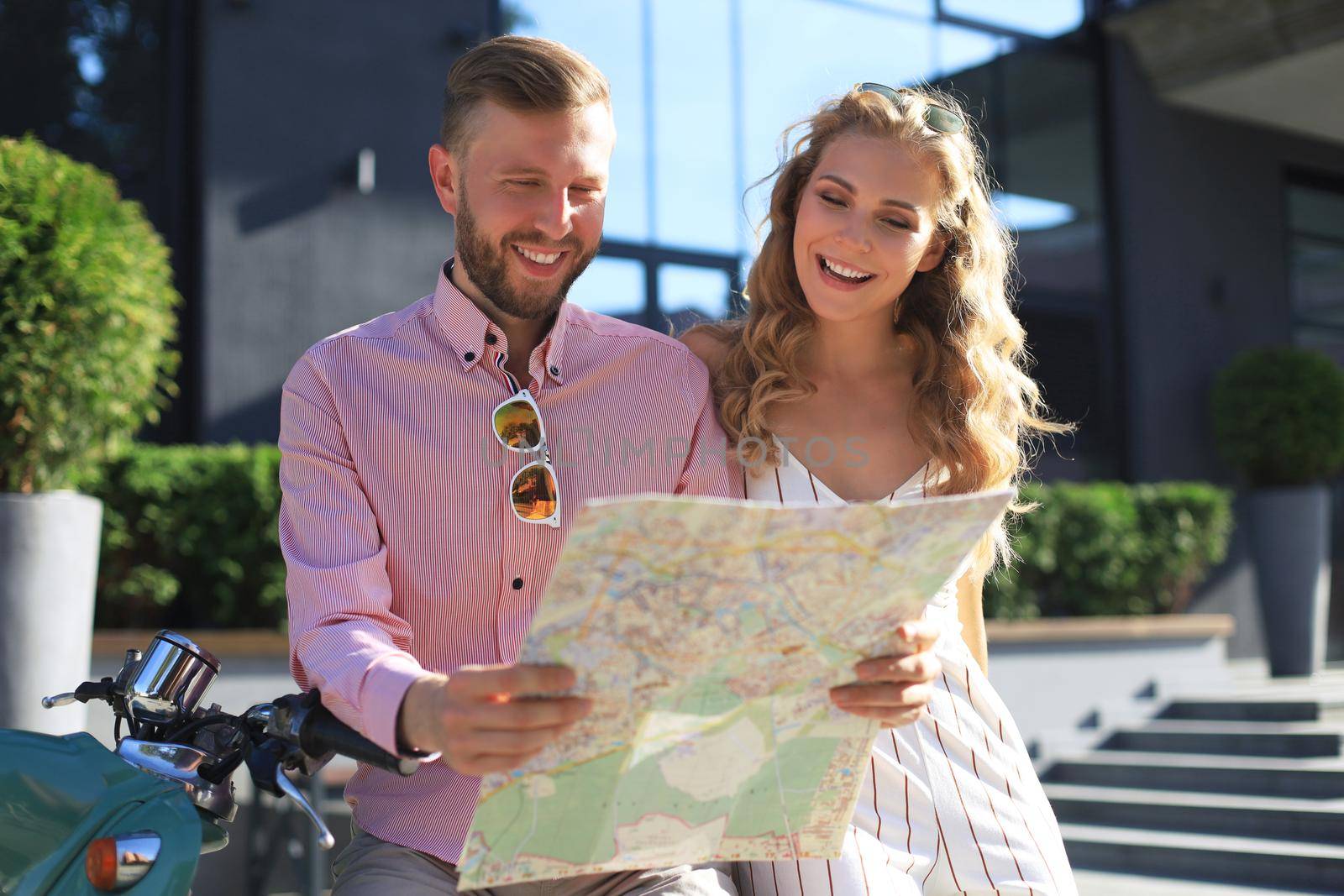 Young happy loving couple looking at map and sitting on scooter