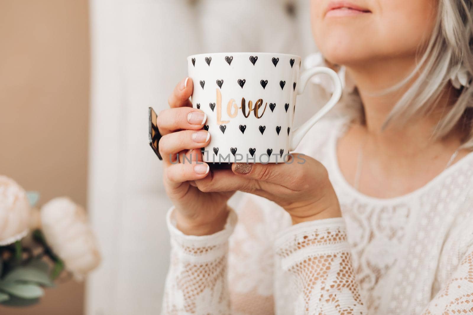 Close-up stock photo of a young fair-haired woman holding a cute coffee cup with golden design and text be mine . Morning coffee in a beautiful coffee cup.