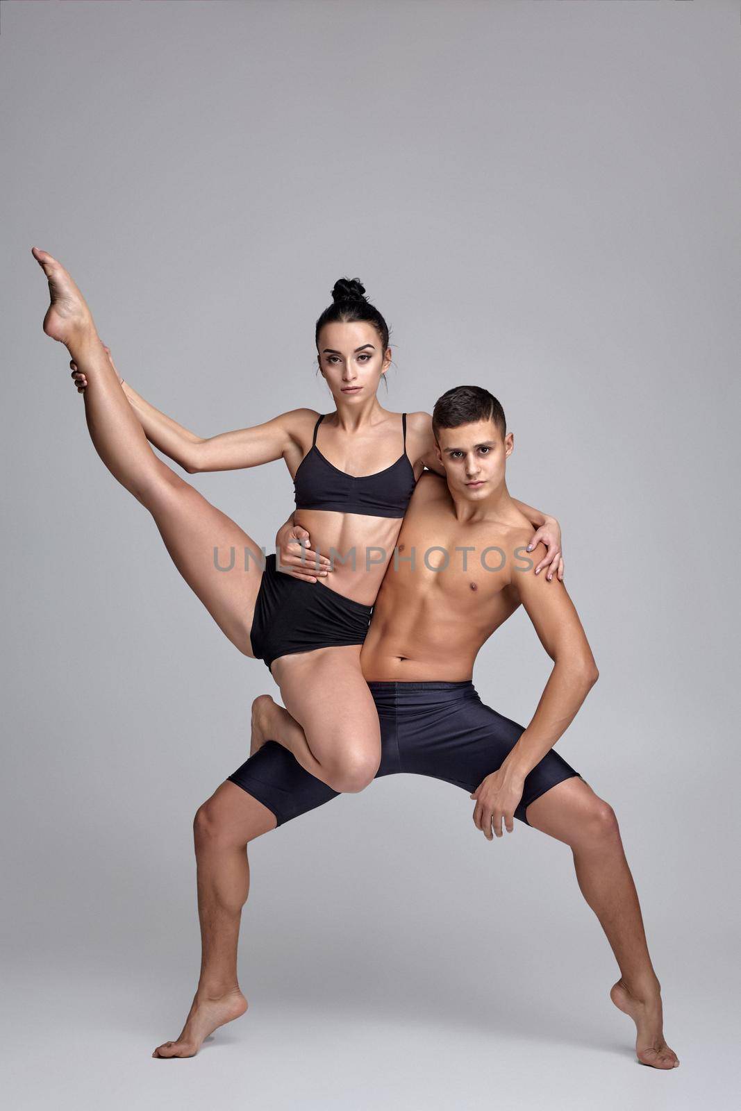 The couple of a young modern ballet dancers in black suits are posing over a gray studio background. by nazarovsergey