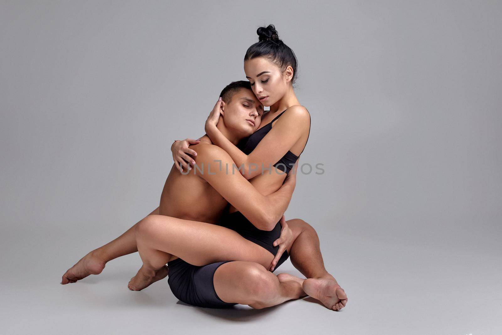 The couple of a young modern ballet dancers in black suits are posing over a gray studio background. by nazarovsergey