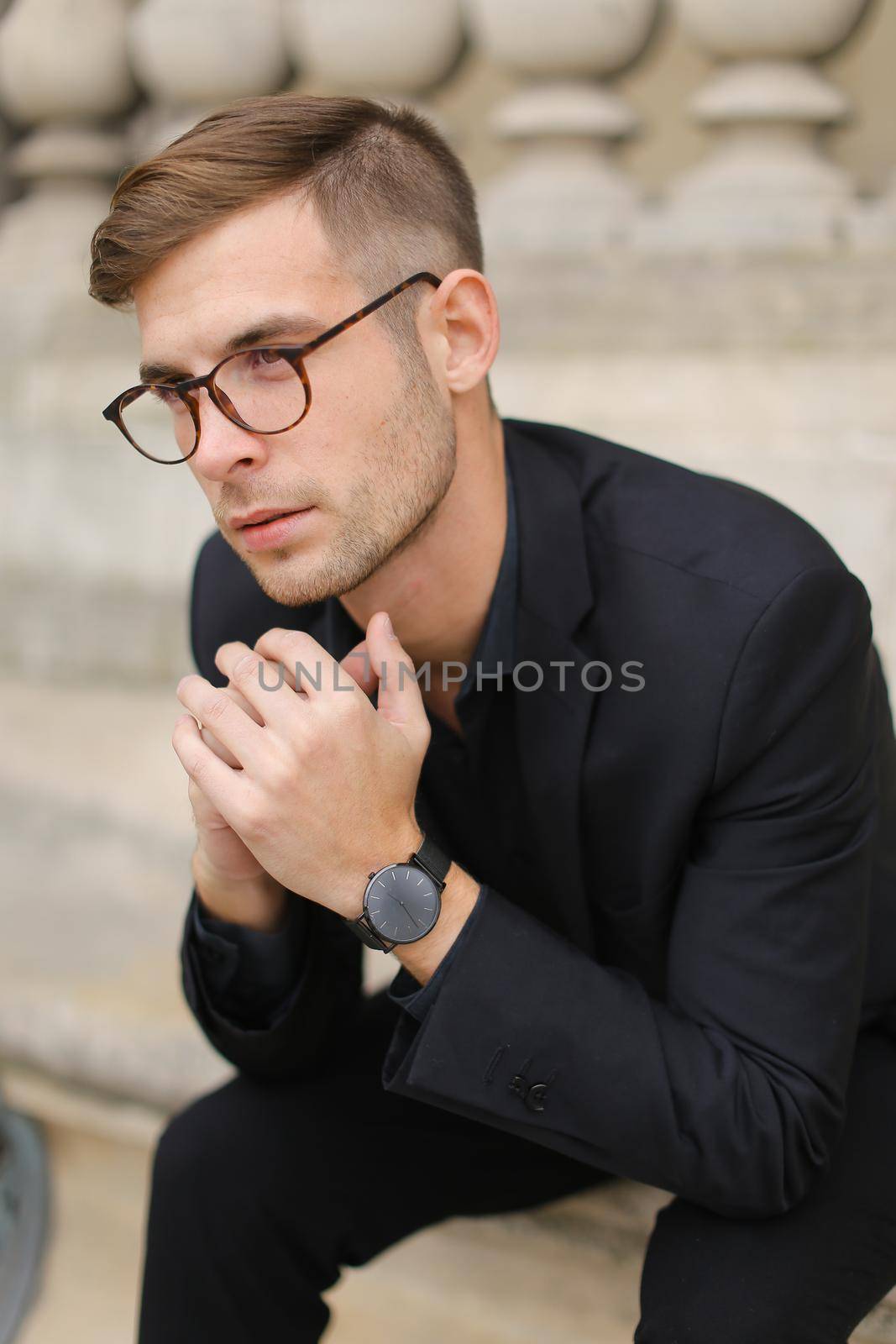 Youn handsome male person sitting on sidewalk leaning on concrete banister. by sisterspro