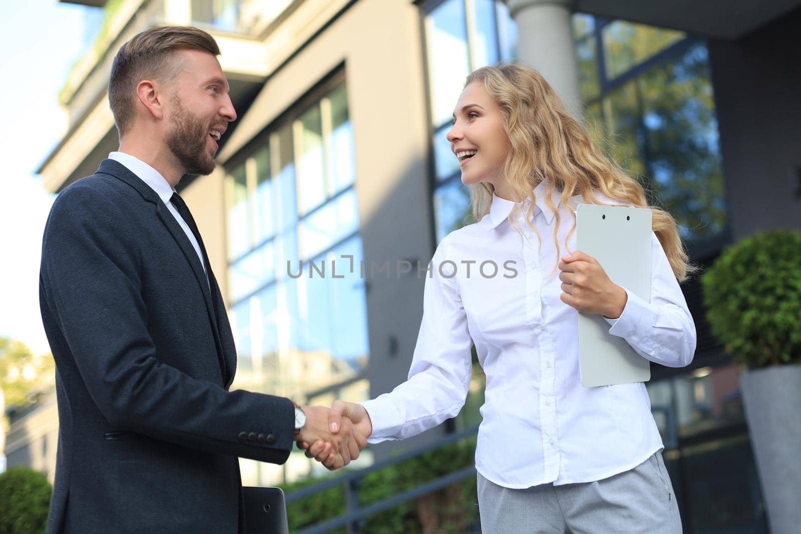 Image of collegues discussing documents and shaking hands near office
