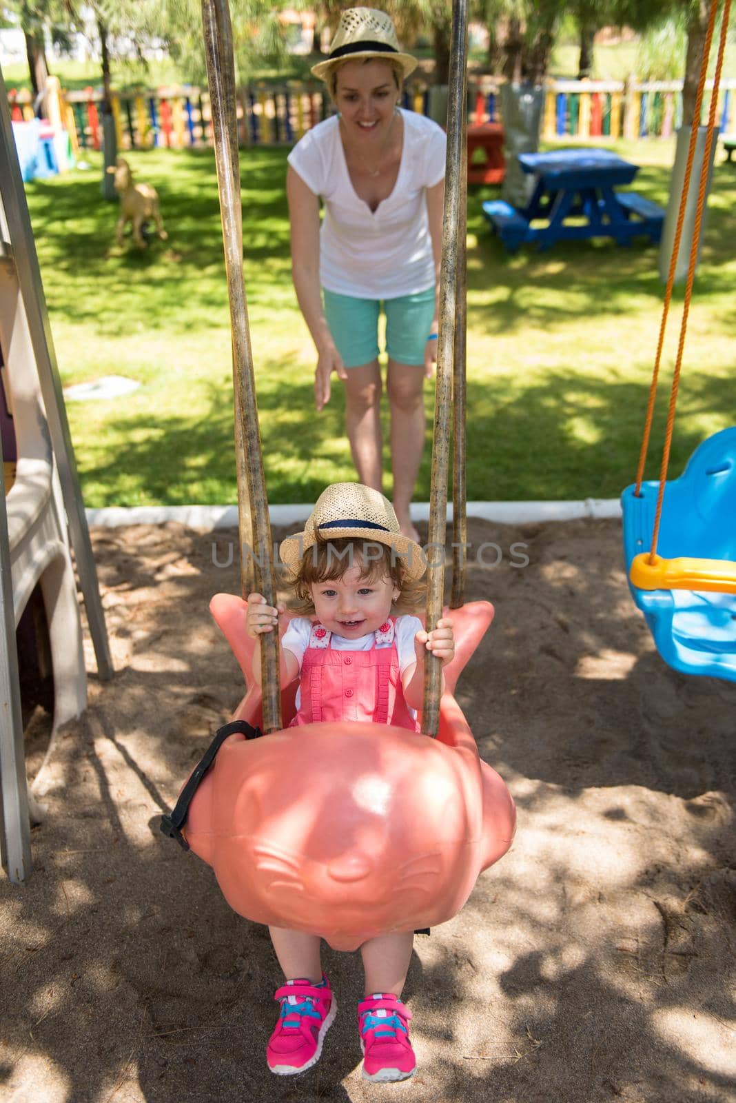 young mother and her little daughter smiling together while swinging at the playground in the park