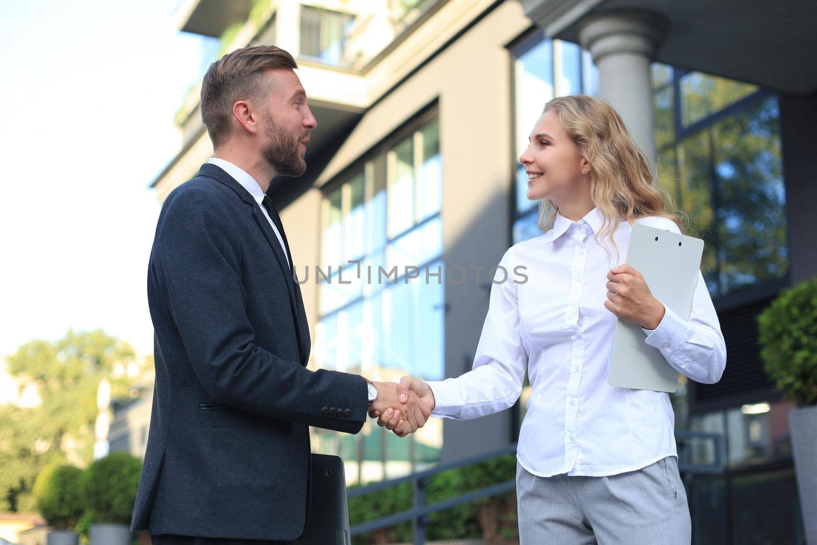 Image of collegues discussing documents and shaking hands near office