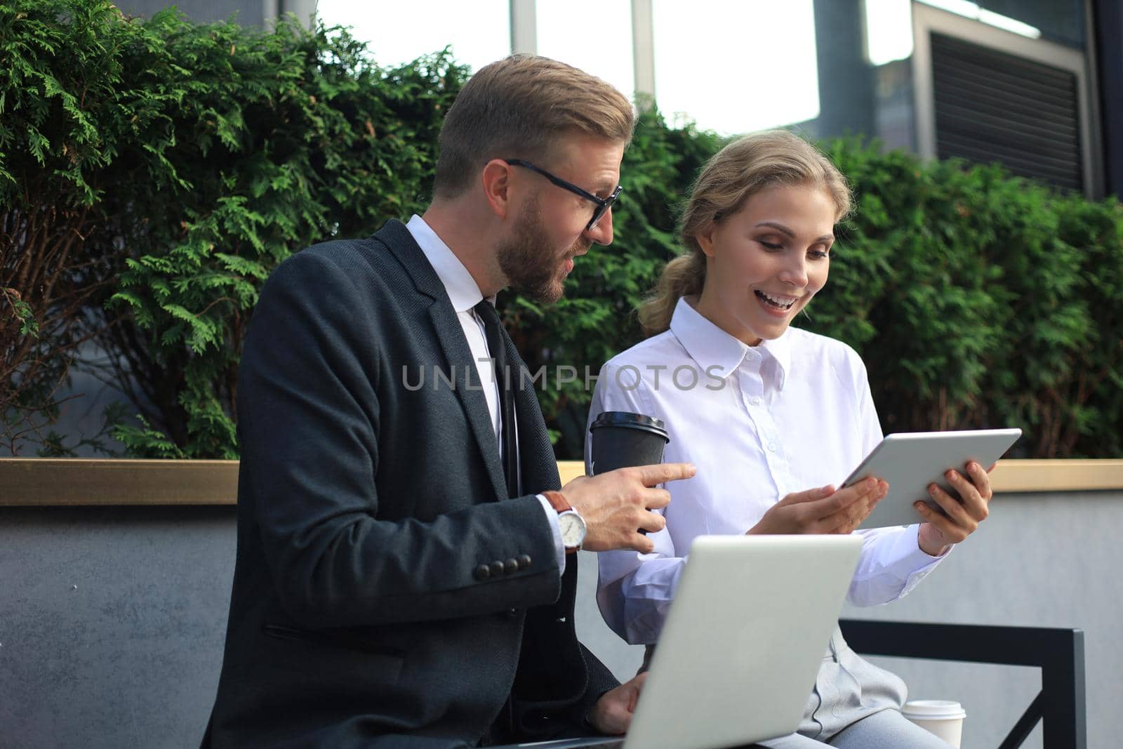 Office colleagues using laptop computer while sitting on a bench outdoors