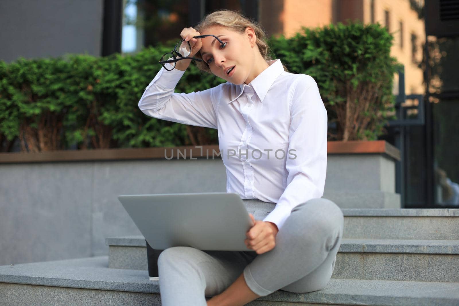 Smiling blonde woman using laptop while sitting outdoors