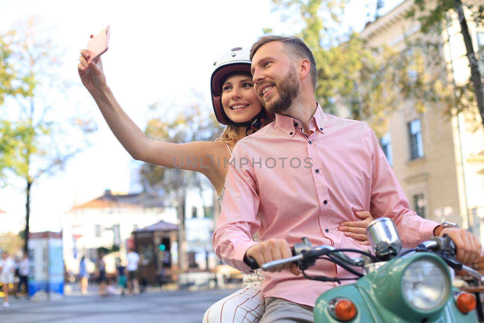 Happy young couple taking selfie on smartphone while sitting on scooter outdoors. by tsyhun