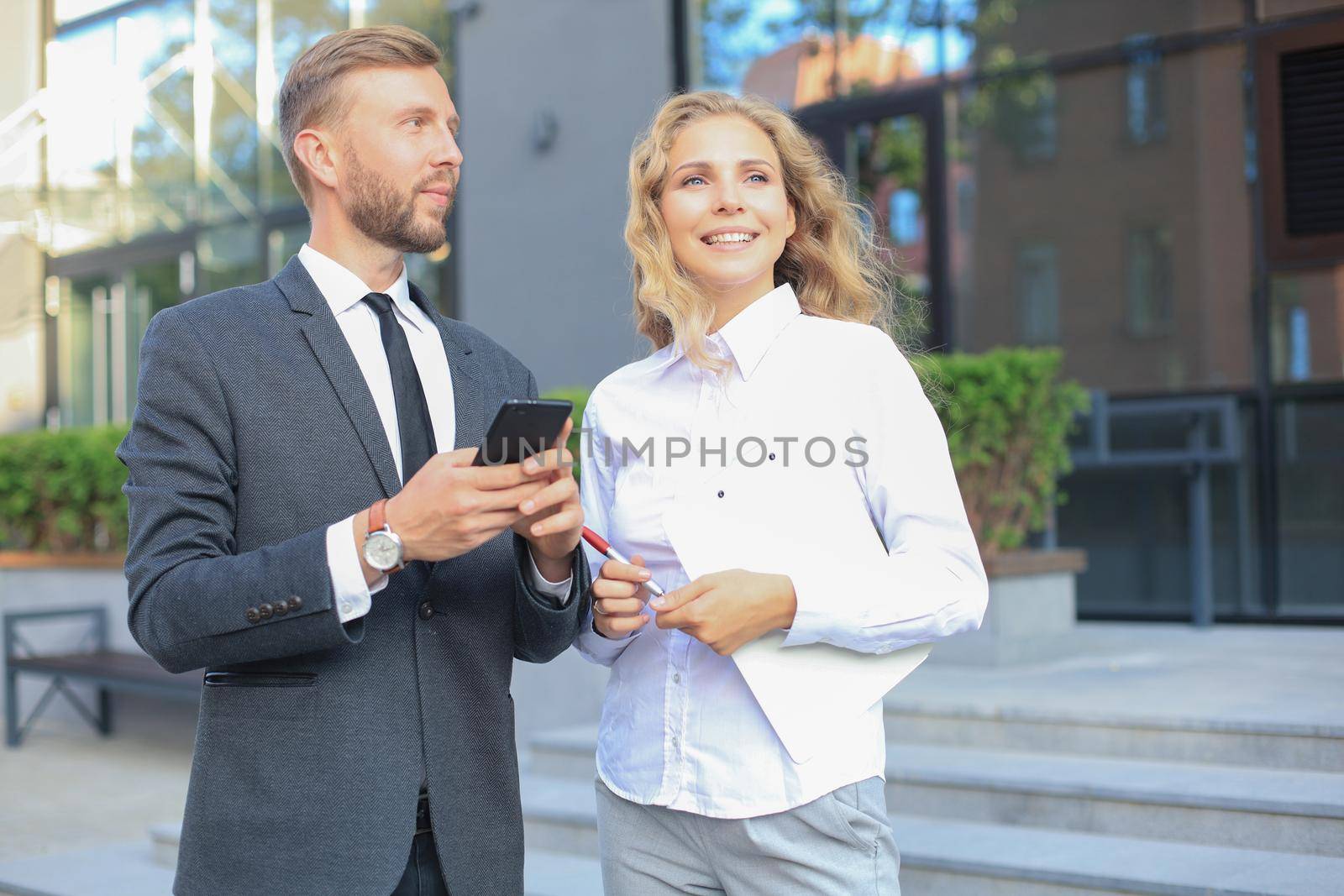 Business colleagues looking at mobile phone standing near office building