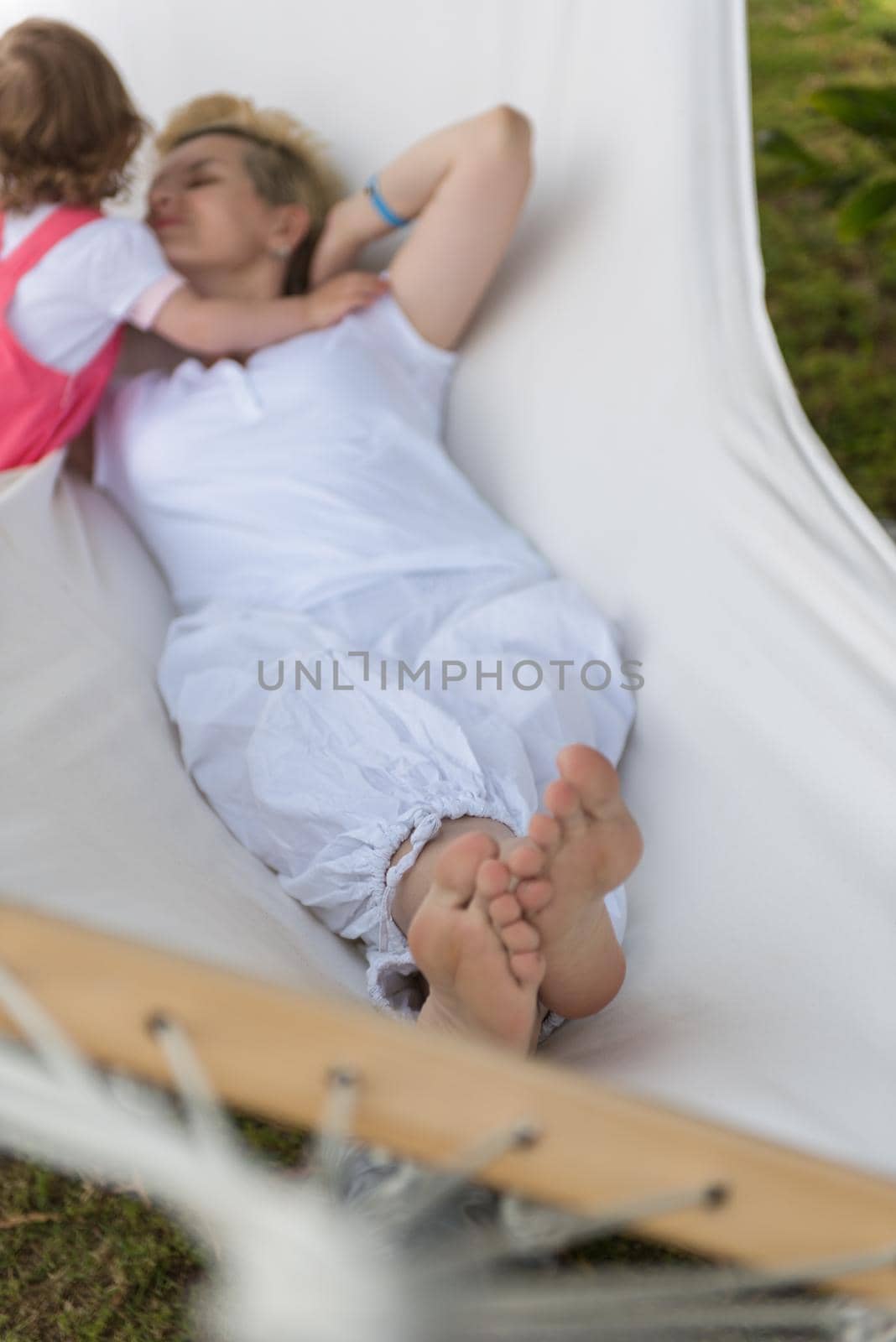 Happy mother and a little daughter enjoying free time hugging and relaxing in a hammock during a sunny day on holiday home garden