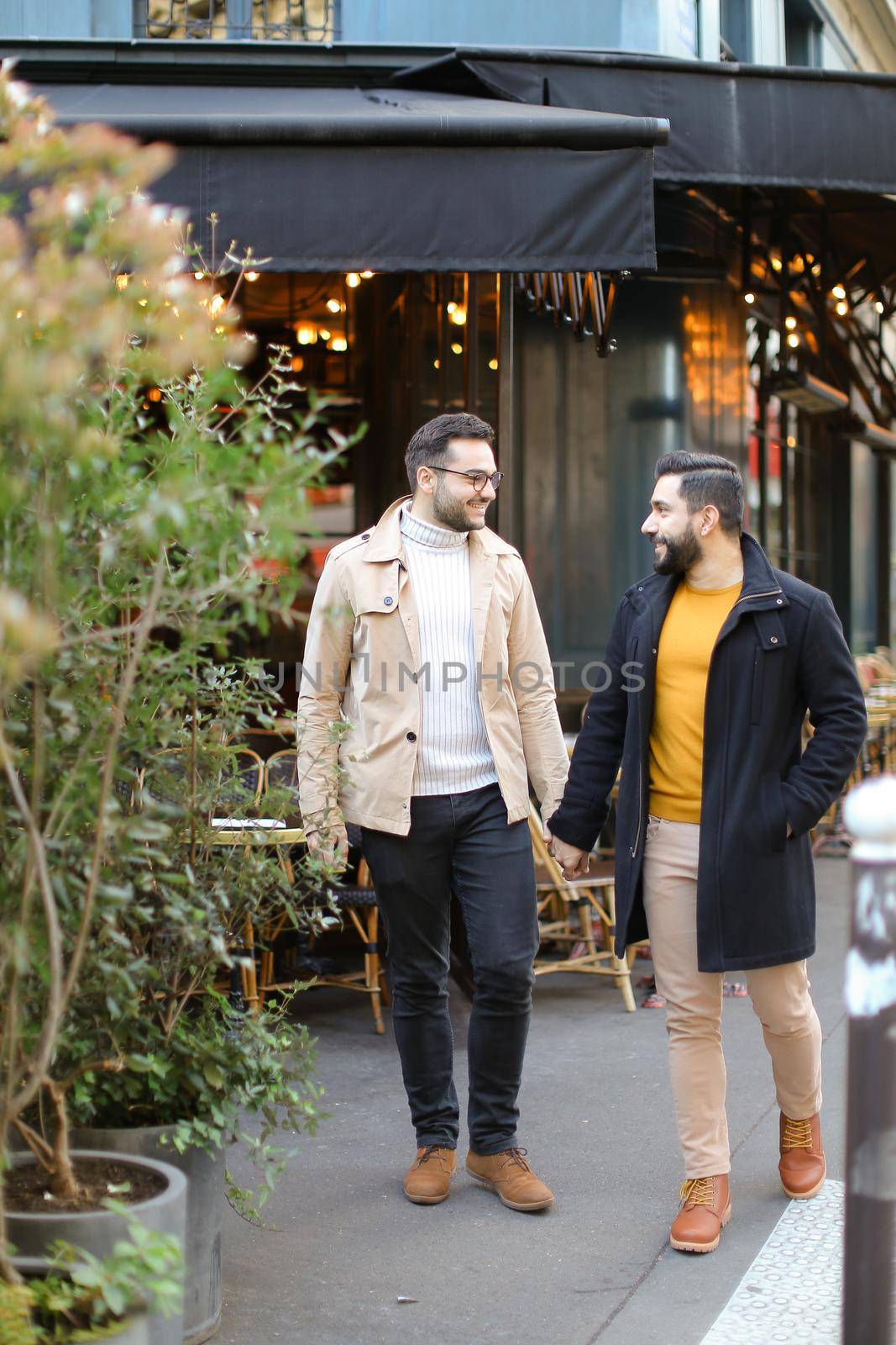 Two young gays standing at street cafe and holding hands. Concept of same sex couple and male friendship.