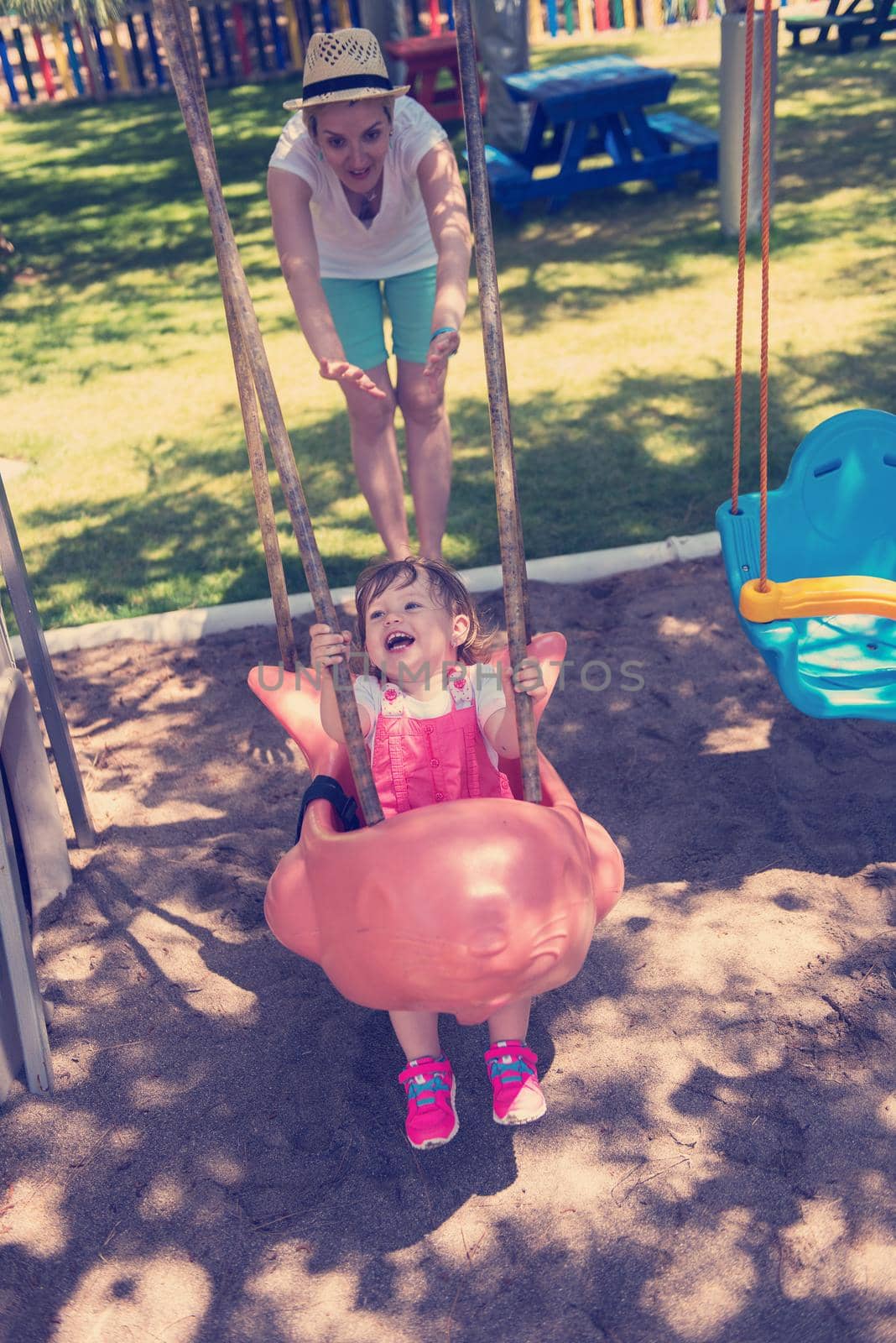 young mother and her little daughter smiling together while swinging at the playground in the park