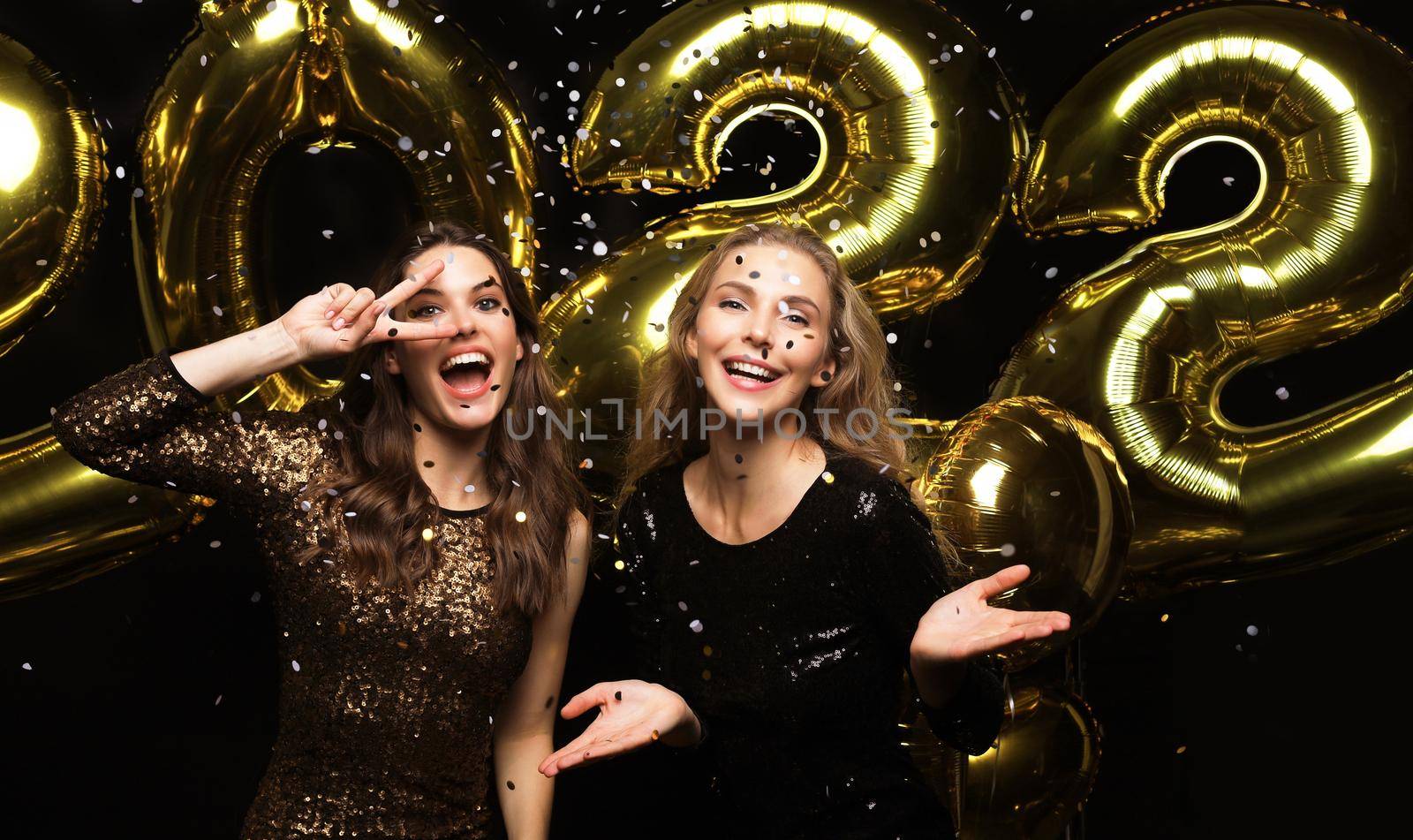 Happy gorgeous girls in stylish sexy party dresses holding gold 2022 balloons, having fun at Christmas or New Year's Eve Party. by tsyhun