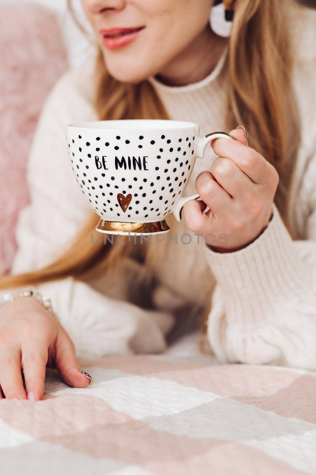 Close-up stock photo of a young fair-haired woman holding a cute coffee cup with golden design and text be mine . Morning coffee in a beautiful coffee cup.