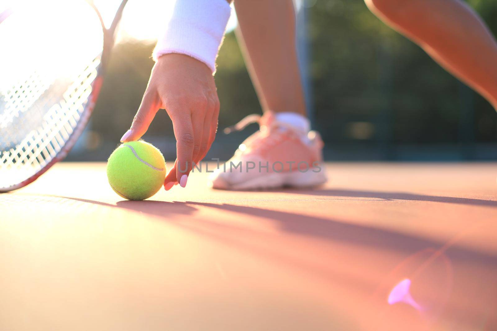 Tennis player raises a tennis ball from the clay court during the game