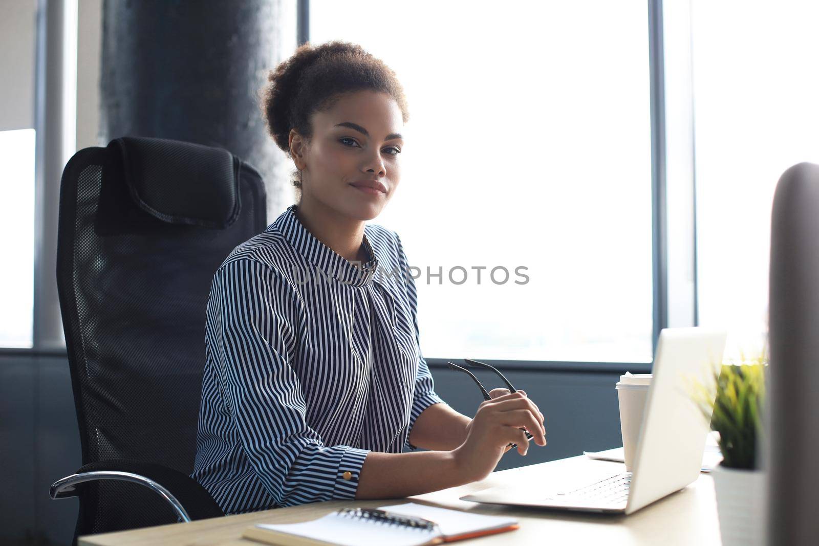 Beautiful young african american woman is sitting in the office and looking at camera