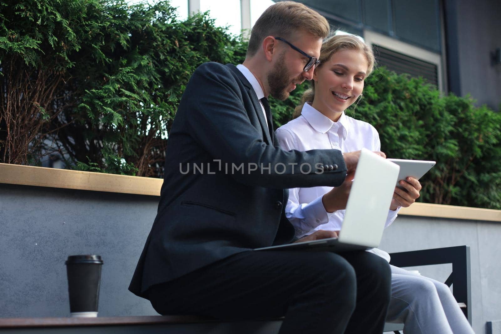 Office colleagues using laptop computer while sitting on a bench outdoors