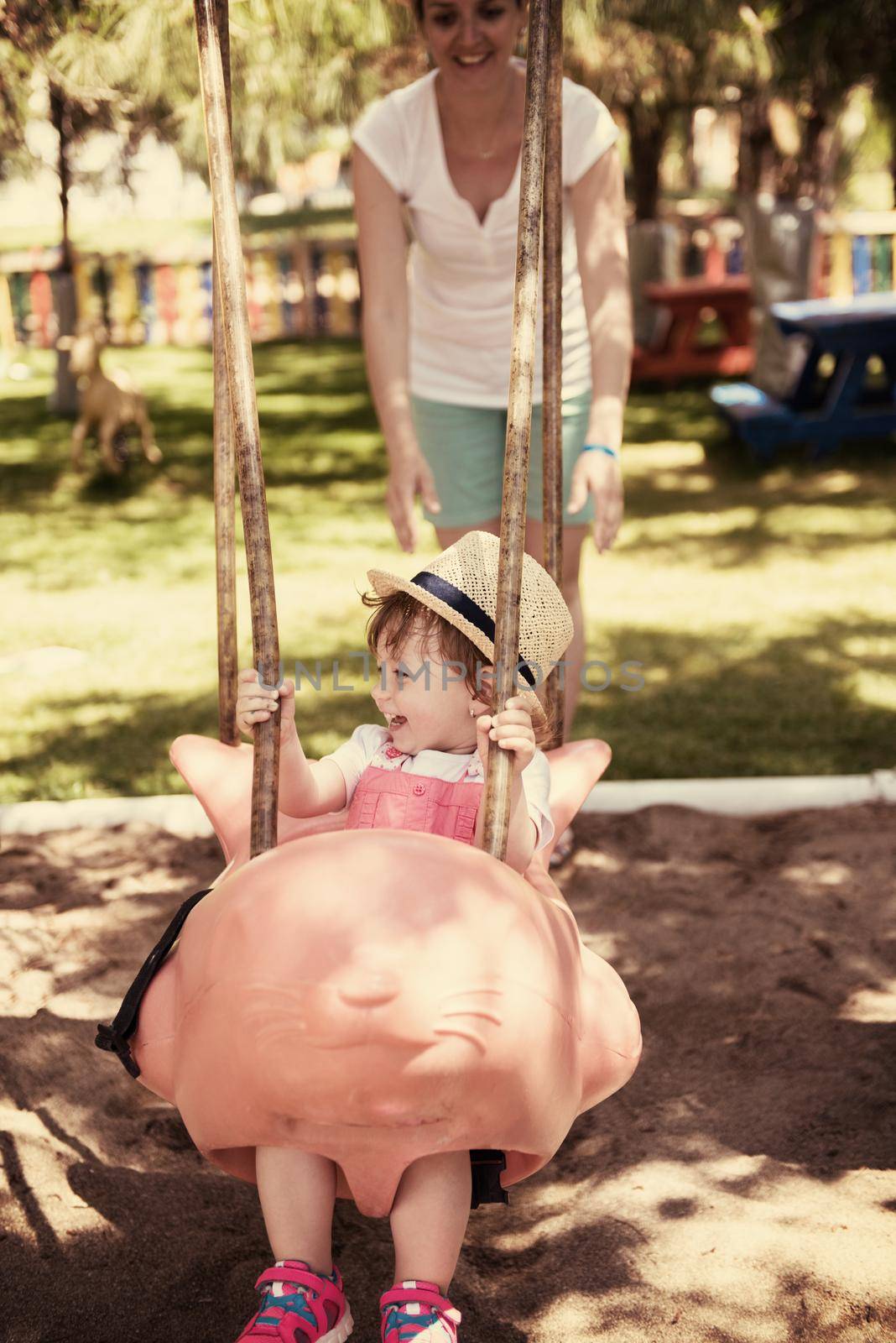 young mother and her little daughter smiling together while swinging at the playground in the park