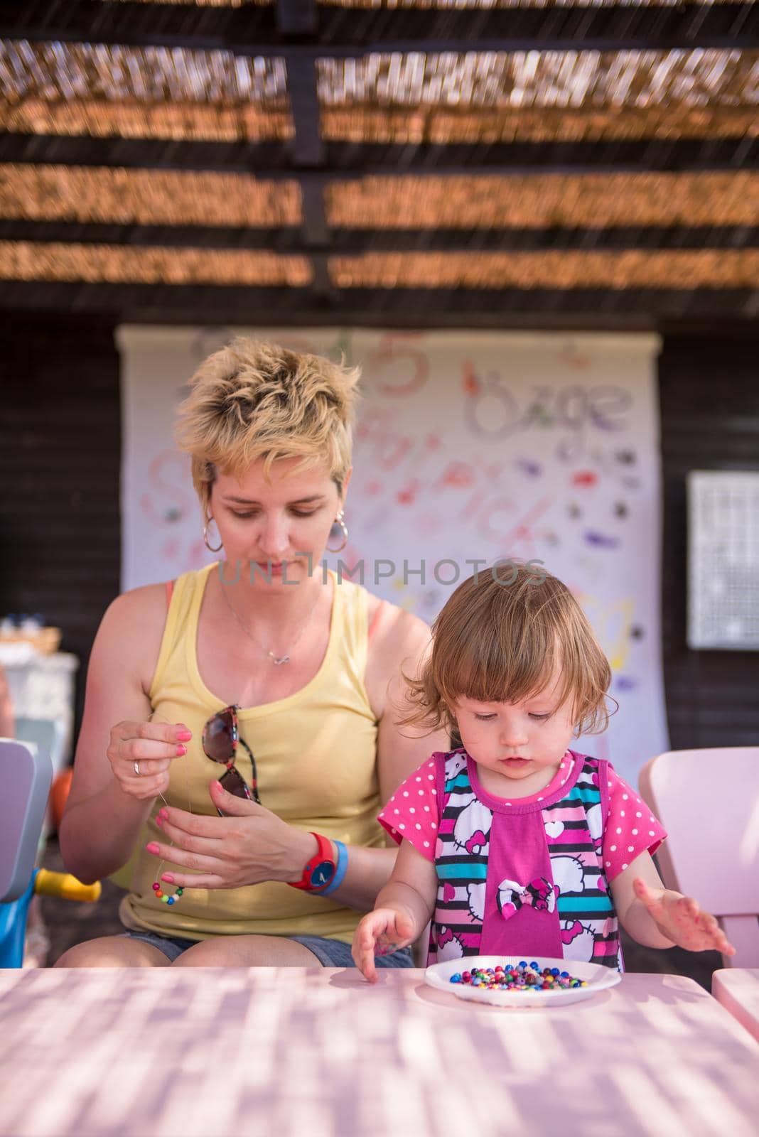 cute little girl making jewelry with  her mother in creative outdoor playground