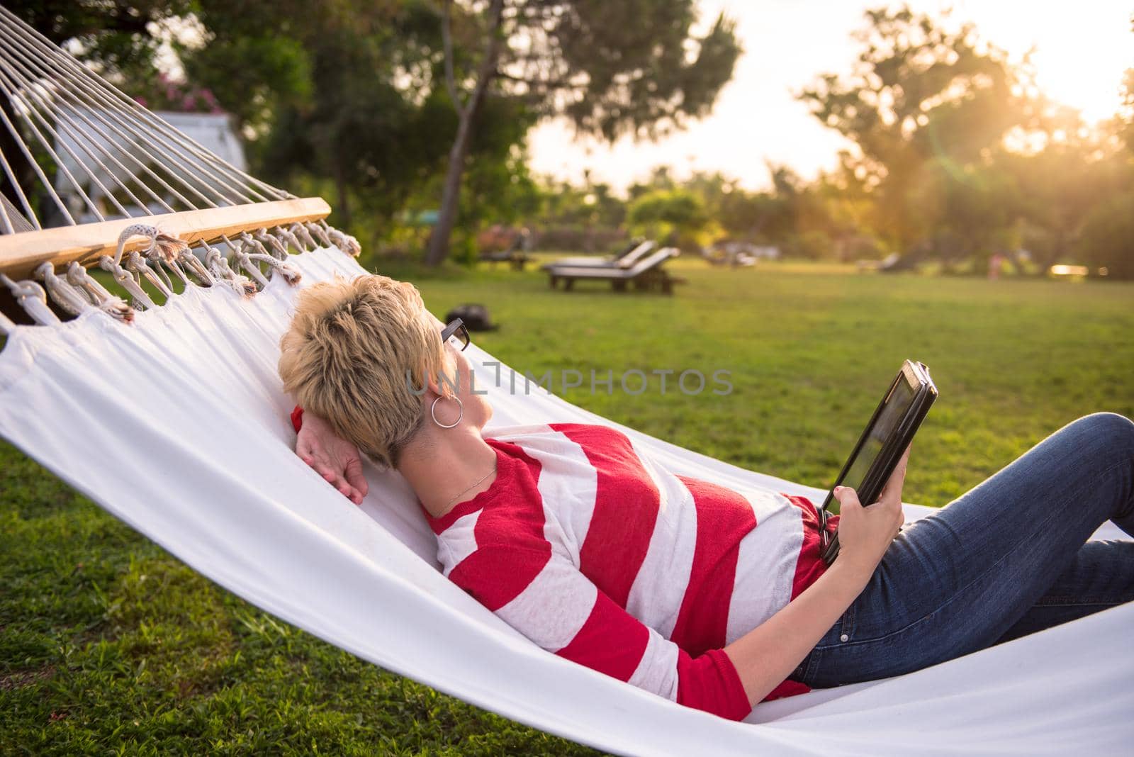 young woman using a tablet computer while relaxing on hammock in a peaceful garden during holiday