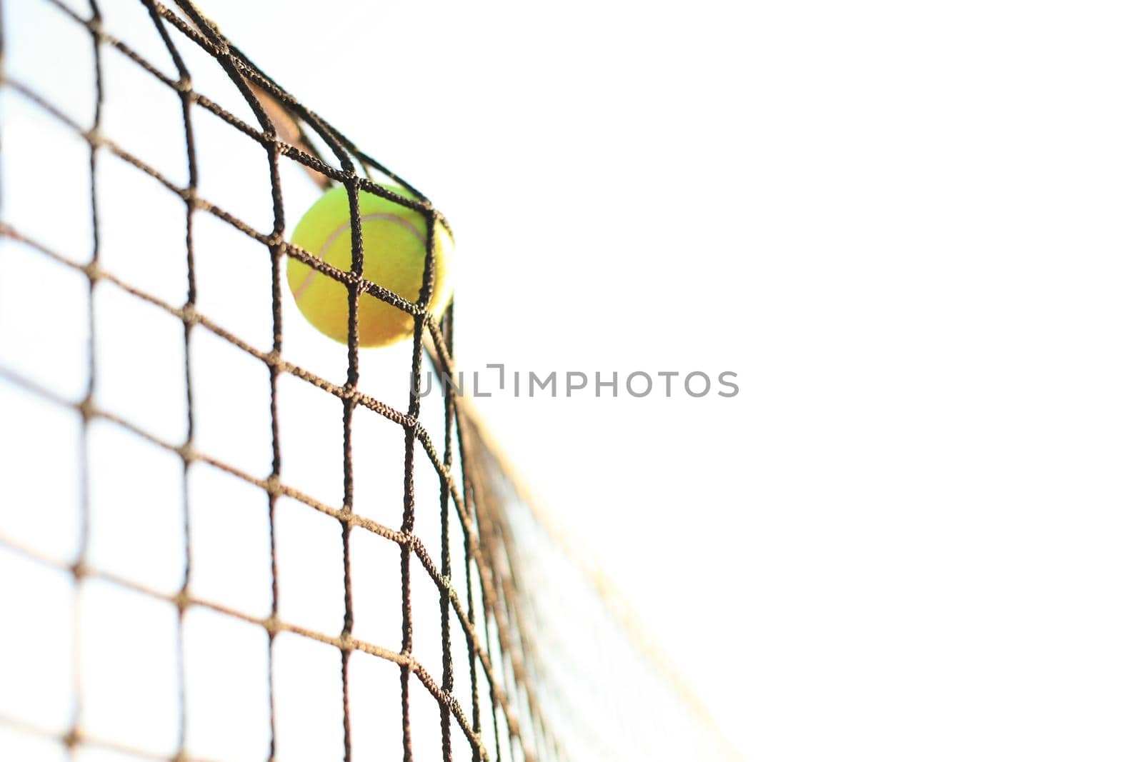 Bright greenish yellow tennis ball hitting the net. by tsyhun