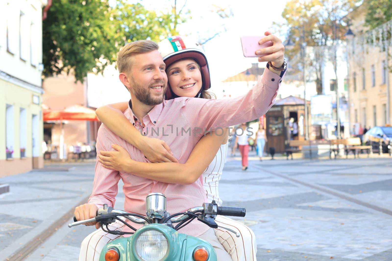 Happy young couple taking selfie on smartphone while sitting on scooter outdoors. by tsyhun
