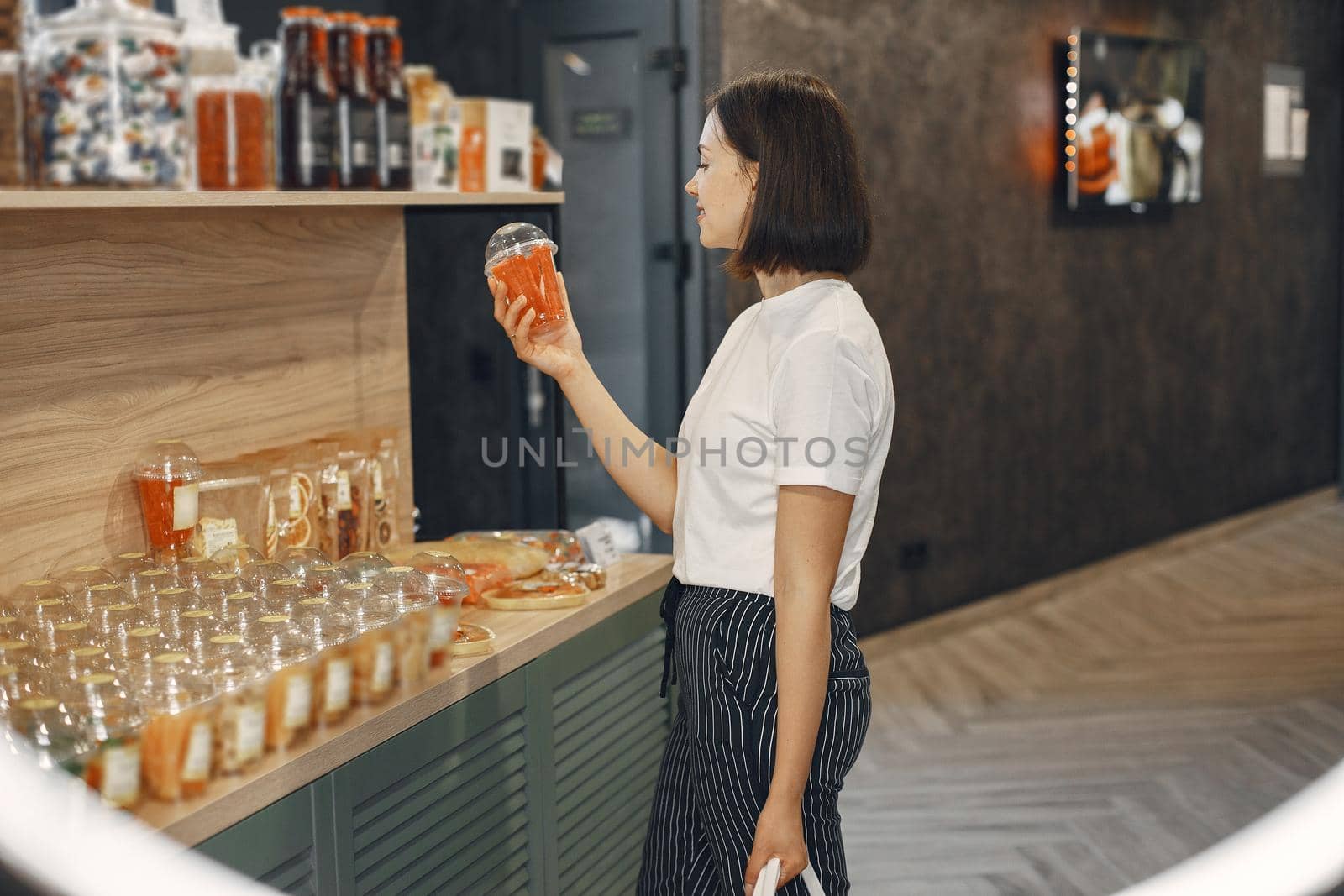 Brunette chooses food. Lady is holding a shopping cart.Girl in a white shirt in the supermarket.
