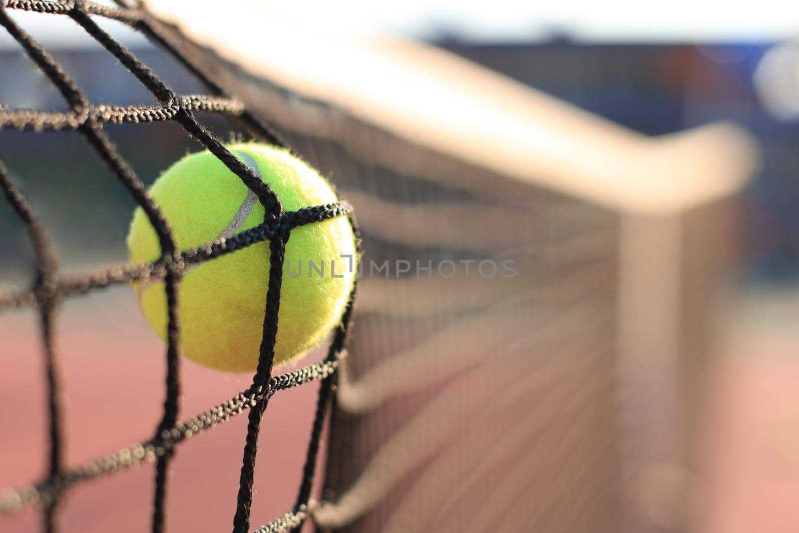 Bright greenish yellow tennis ball hitting the net. by tsyhun