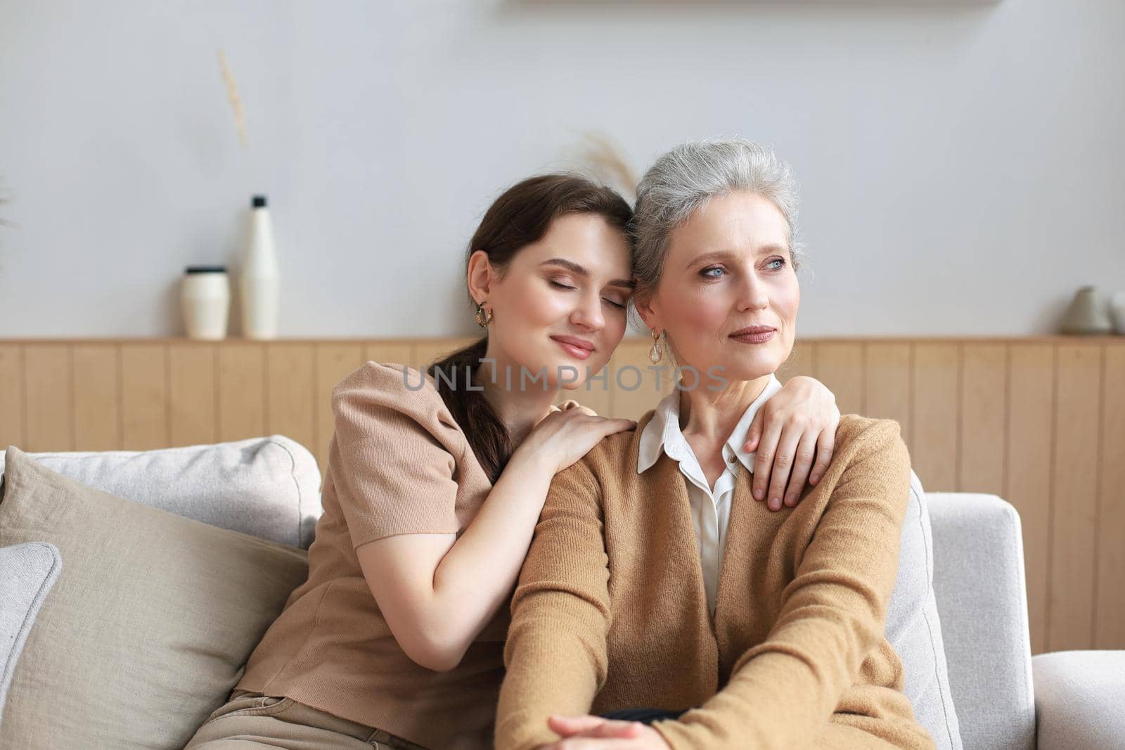 Beautiful mother and daughter. Cheerful young woman is embracing her middle aged mother in living room. Family portrait