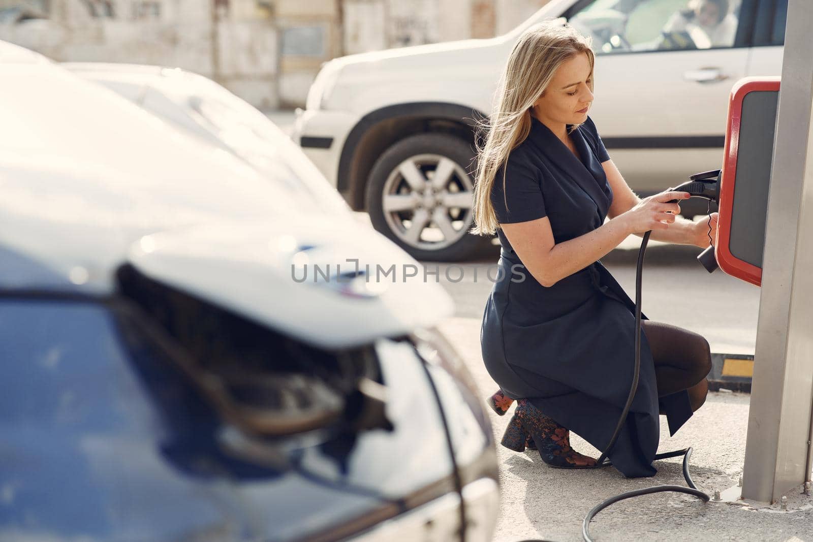 Woman on a gas station. Lady in a blue dress. Woman near the car.