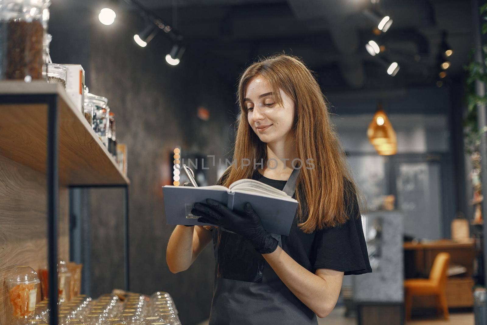 Brunette holding a notebook. Woman in apron. Lady in the store.