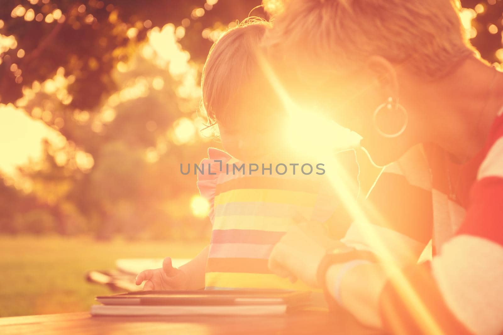 Happy mother and her little daughter enjoying free time using tablet computer while relaxing  on holiday home garden during sunny day