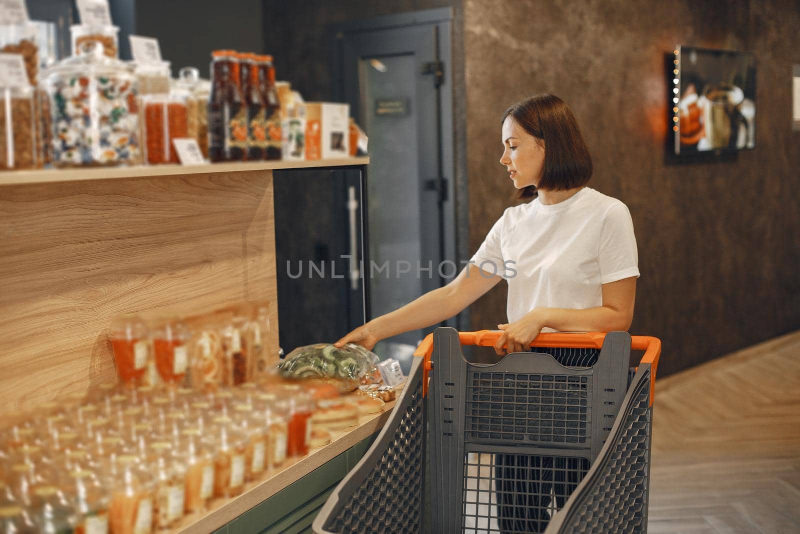 Brunette chooses food. Lady is holding a shopping cart.Girl in a white shirt in the supermarket.