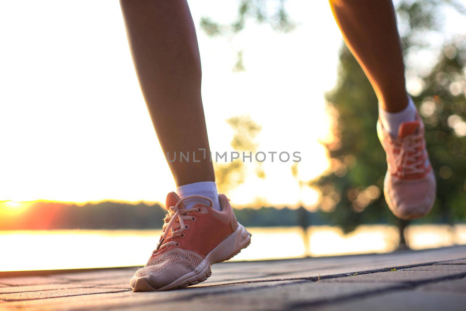 Woman runner legs and shoes in action on road outdoors at sunset