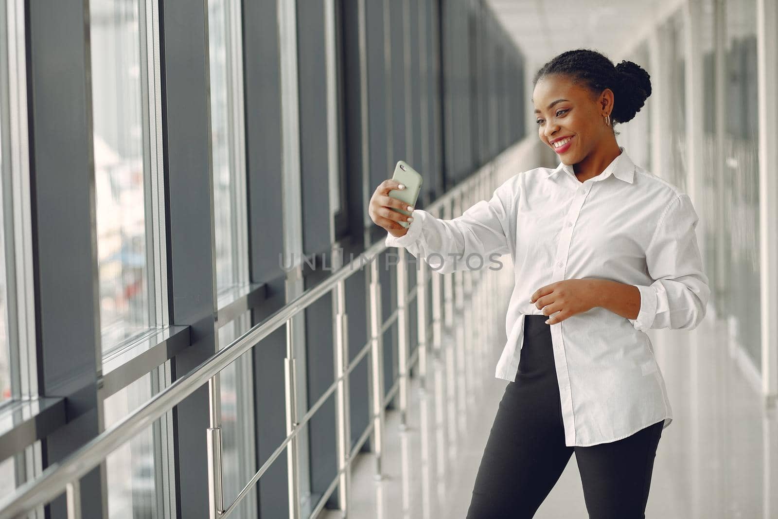 Black girl in the office. Woman in a white shirt. Lady use the phone.