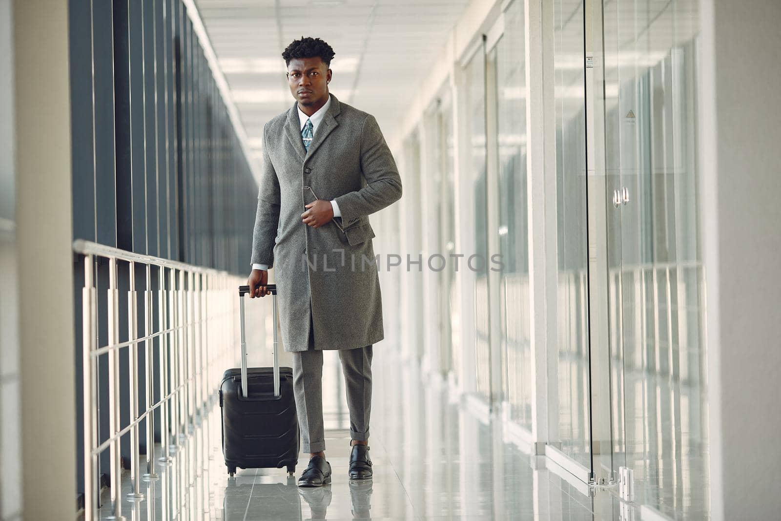 Elegant black man at the airport with a suitcase by prostooleh