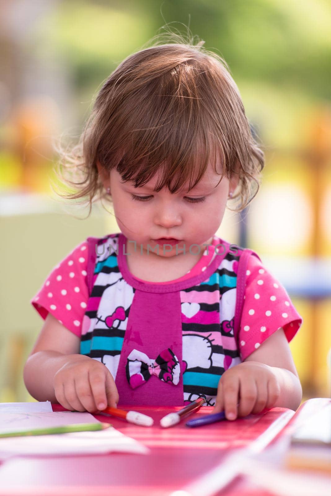 cute little girl cheerfully spending time using pencil crayons while drawing a colorful pictures in the outside playschool