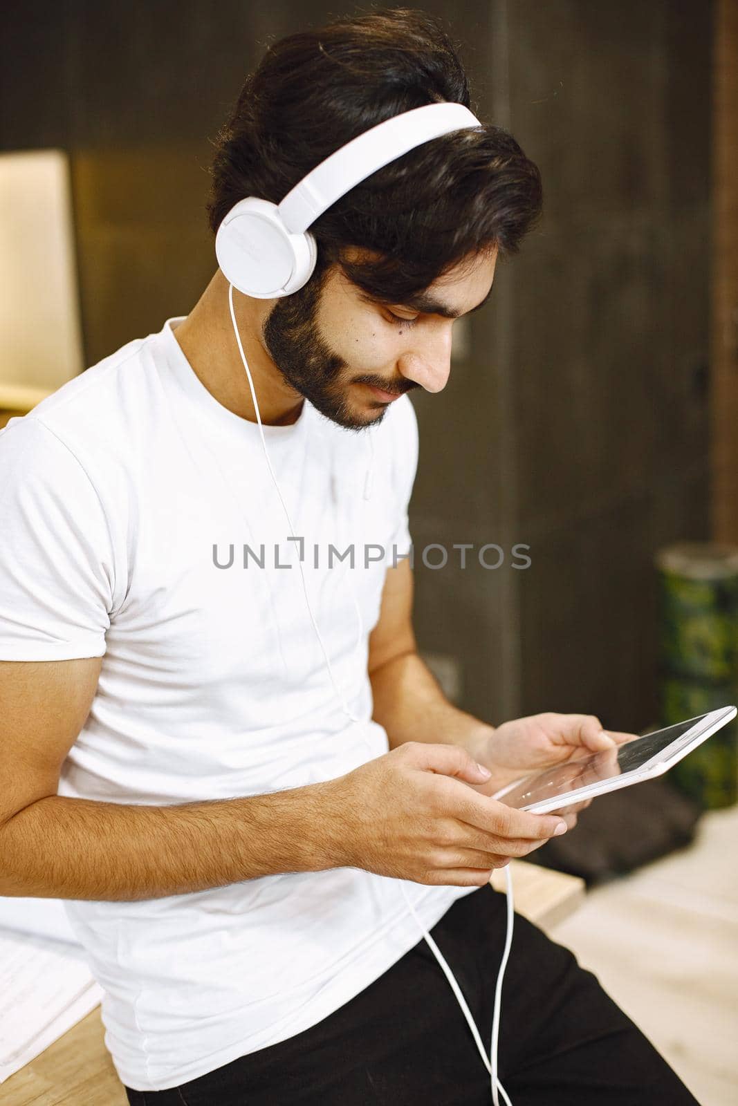 Arabic man watching online webinar, sitting in a kitchen with a tablet enjoying distance learning.