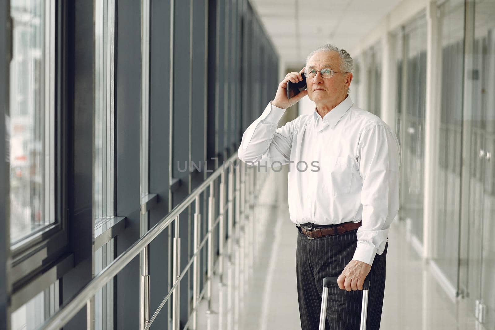 Man at the airport. Senior with suitcase. Male in a white shirt.