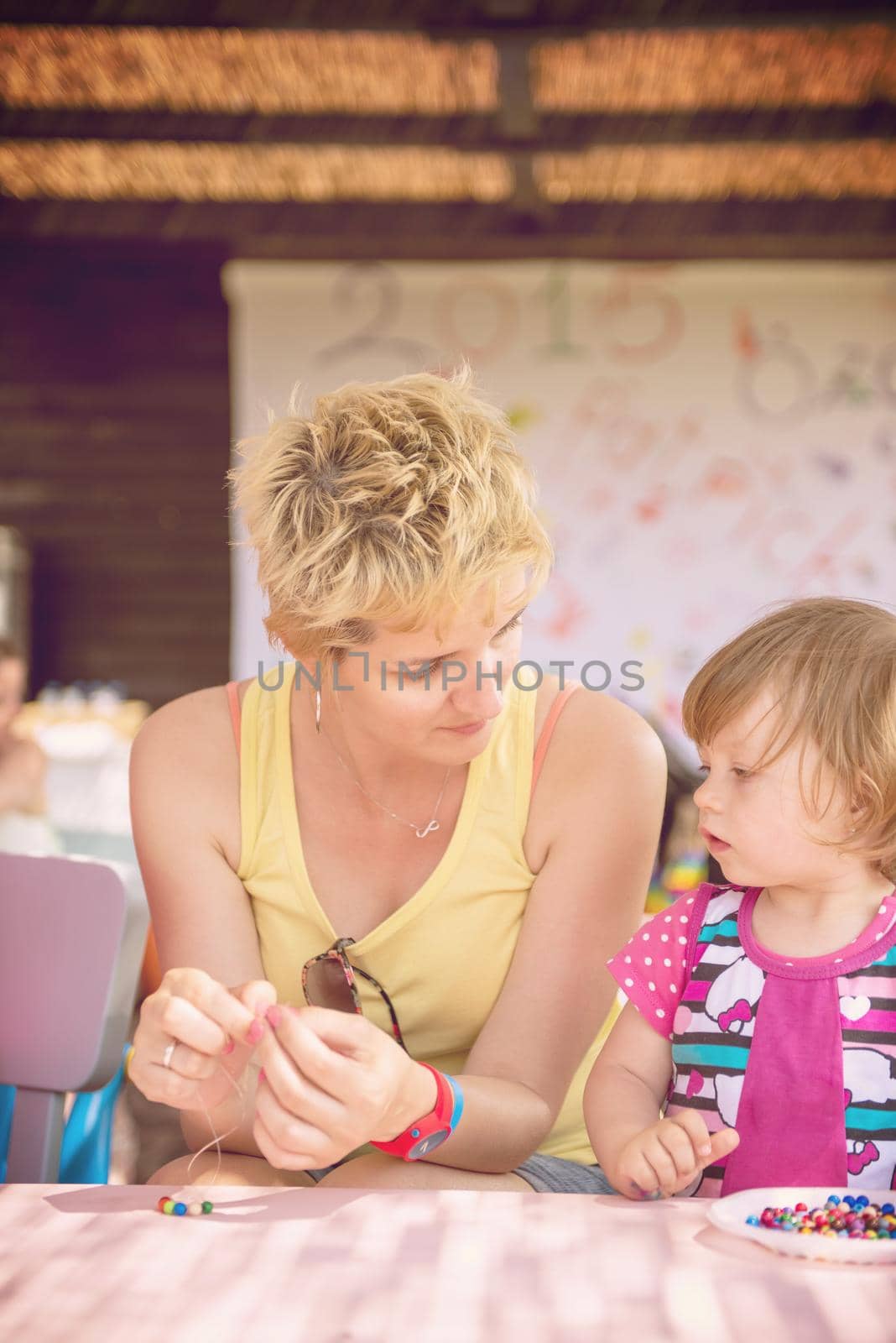 cute little girl making jewelry with  her mother in creative outdoor playground