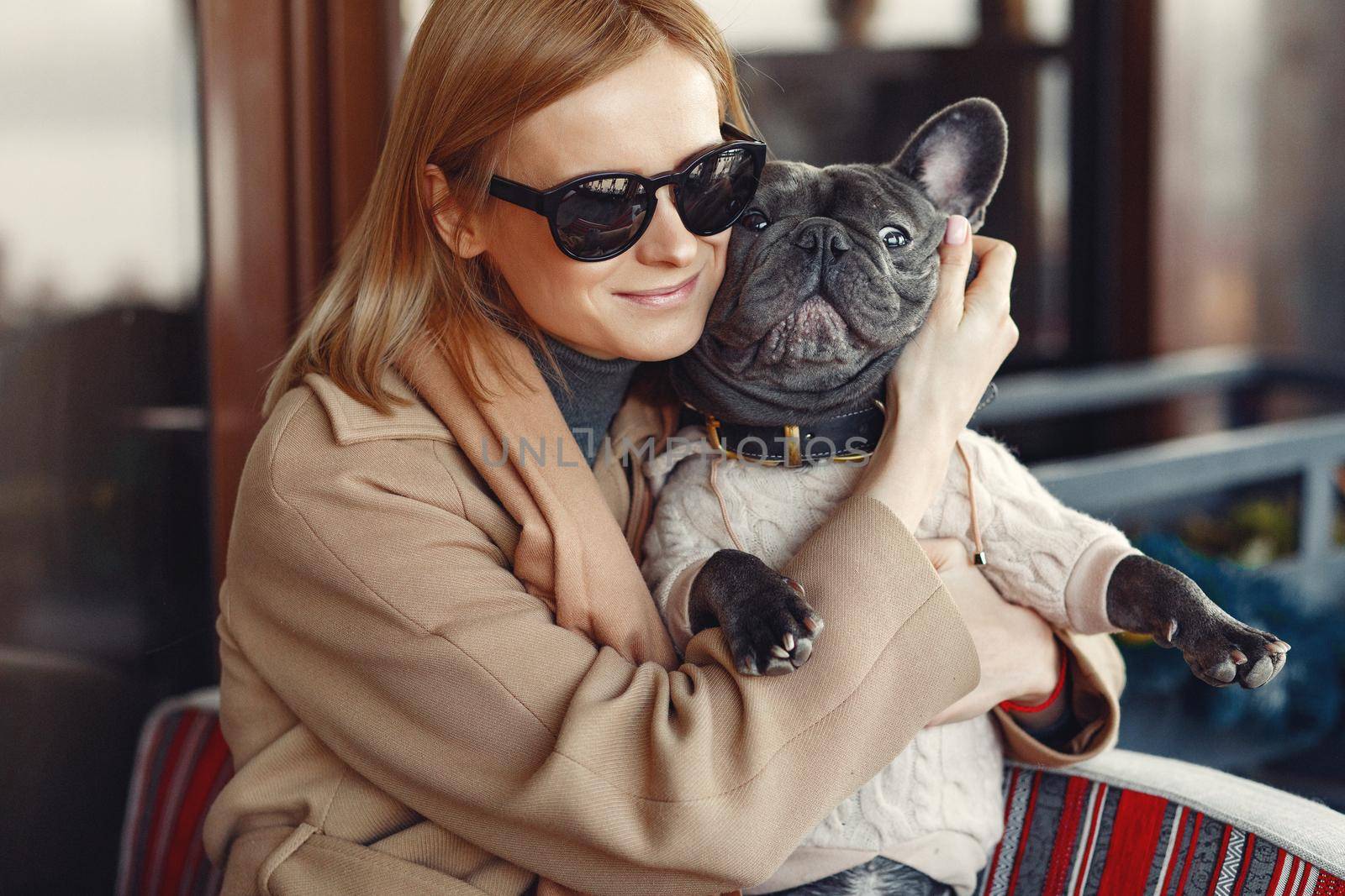 Woman with dog. Lady in a brown coat. Girl play with bulldog. Woman in a cafe.