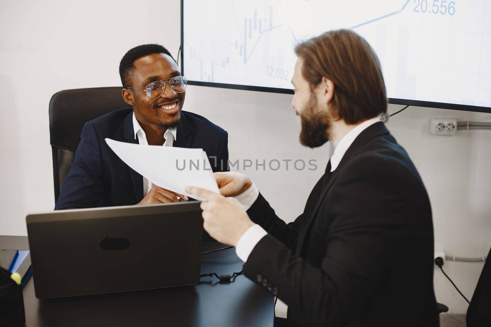 African man in a black suit. International partners. People sitting at the table with laptop.