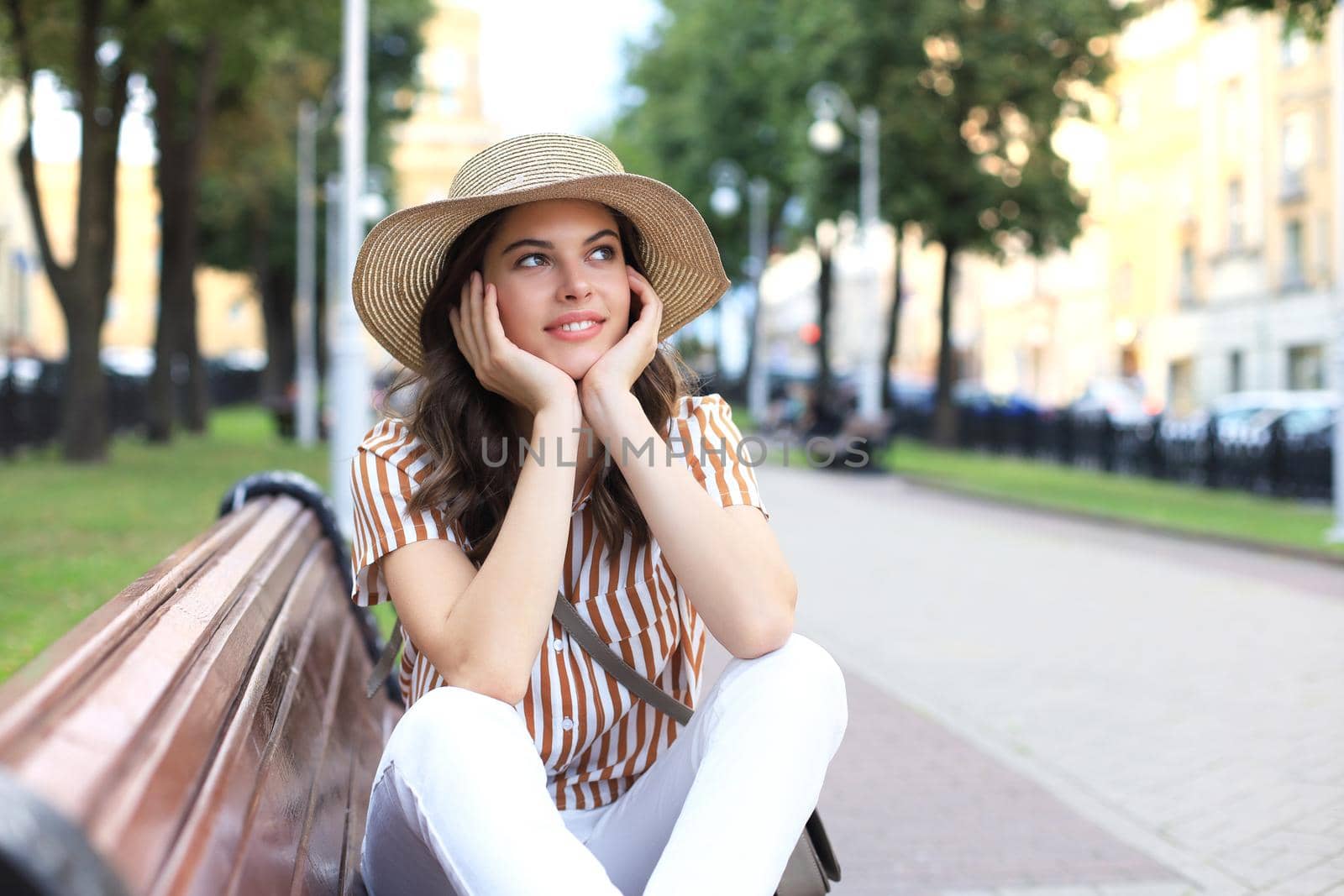 Beautiful smiling young brunette woman sitting on bench in park